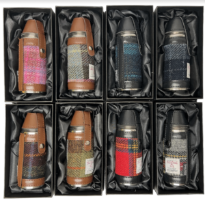 alt= a collection of hunting flasks with two different styles of leather brown and black and eight different harris tweed patterns on a white background