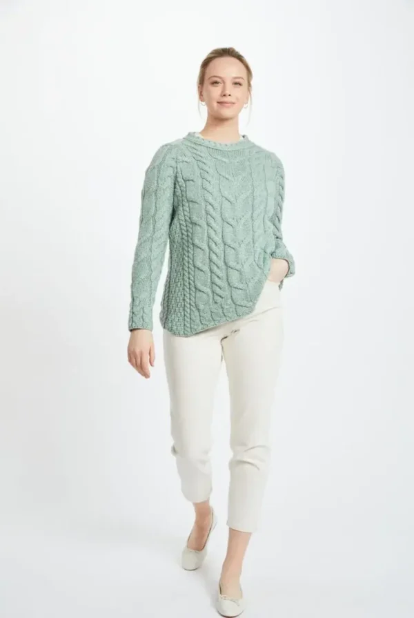 Irish woman in a light blue Aran Raglan sweater with cable-knit patterns, white pants; crafted wool, heritage warmth, timeless style.