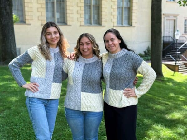 Three women in Irish Aran sweaters with classic cable knit, soft gray and cream wool; iconic for heritage warmth and coastal tradition.