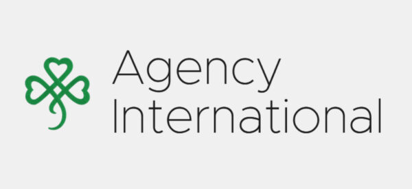 Irish-inspired green shamrock logo with heart motifs beside bold Agency International text; evokes Celtic heritage and goodwill.