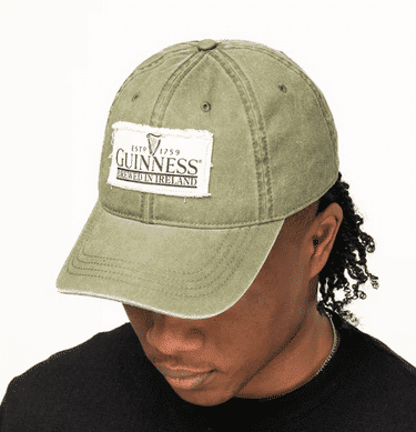 Irish-inspired olive green wool flat cap (Guin GN9039) with classic patchwork, worn by curly-haired person in black shirt.