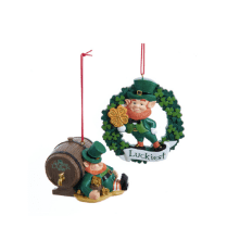 Irish leprechaun ornaments: one by wood barrel, one with shamrock wreath, clover, “Luckiest” banner; vibrant hand-painted ceramic.