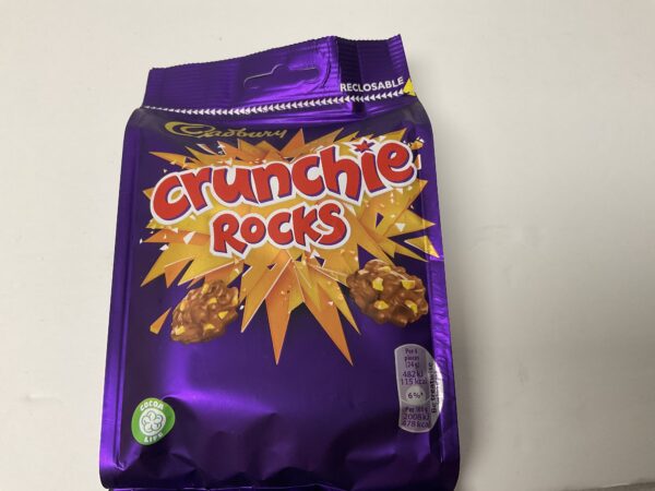 Sure! However, Crunchie Rocks is a product by Cadbury—a company with roots in Birmingham, England rather than Celtic nations. Still, Ill infuse the alt text with as much heritage-focused detail and cultural resonance as possible within your constraints: Cadbury Crunchie Rocks 110g pack; golden honeycomb clusters on rich purple wrapper, echoing British confectionery tradition. Let me know if youd like it tailored further to reference any specific UK traditions or motifs!