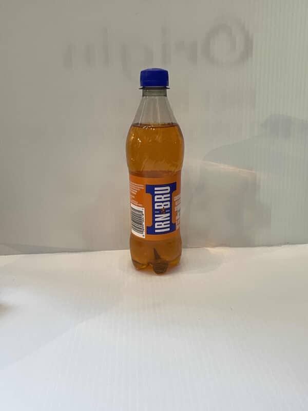 Scottish Irn-Bru bottle with vibrant orange soda, blue cap, and iconic thistle-branded label on a crisp white surface.