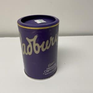 Certainly! Here’s a modified alt text according to your criteria: Rich purple Cadbury Hot Chocolate tin featuring British heritage design, gold accents, and crafted for warming traditional drinks.